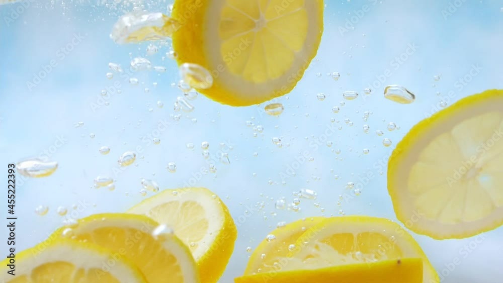 Slow Motion of fresh yellow lemon slices falling into water splash on blue background, Vegetables for health.