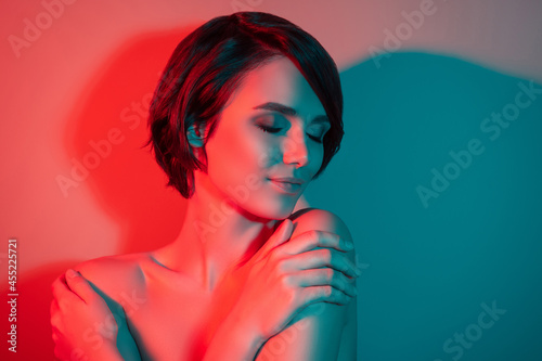 Photo of relaxed joyful dreamy stunning short hairstyle woman hug herself isolated red neon light color background