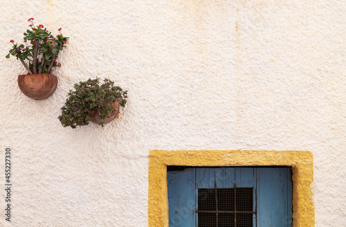Windows with yellow frame, blue door and traditional Spanish flowerpots on white wall in Nijar, Andalusia, Spain