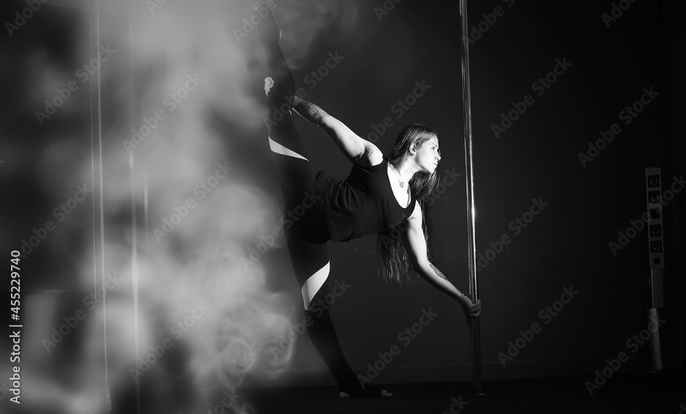 The dancer on the pylon in the studio. Girl doing exercises on a sports equipment.