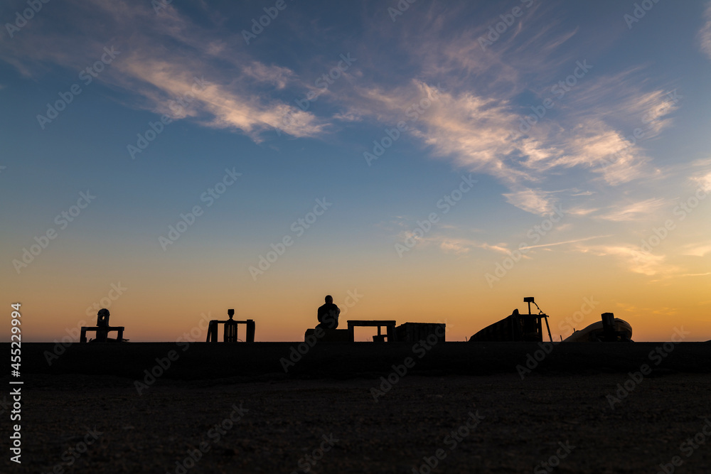 Naklejka premium Silhouette of adult man looking at view on beach with fishing boat and winch during sunset