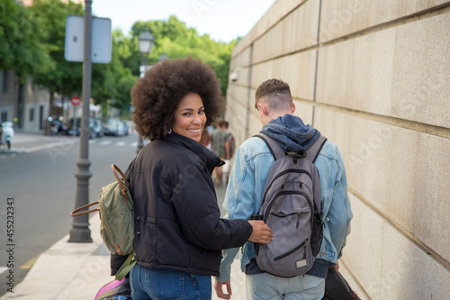 African American woman looking at camera and Caucasian man walking through the city with a motorcycle helmet in hand