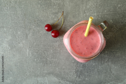 Glass jar of cherry smoothie and ingredients on gray textured table