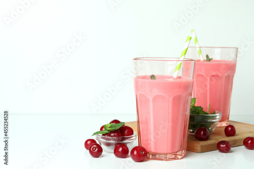 Glasses of cherry smoothie and ingredients on white table