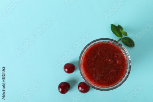 Glass of cherry smoothie and ingredients on blue background