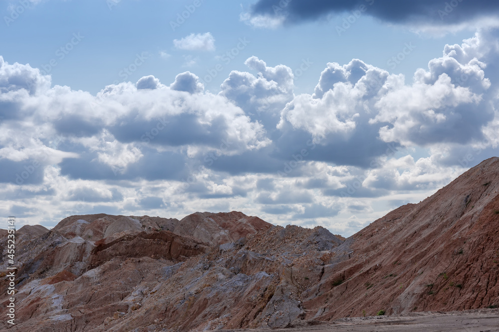 Rock dumps in ilmenite quarry against cloudy sky, backlit