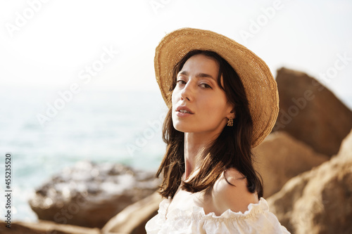 Young joyful brunette woman posing against sea and rocks