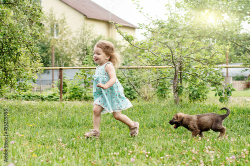a little girl with curly hair is playing with a German Shepherd puppy, laughing, rejoicing on the green grass. happy childhood. summer holidays.