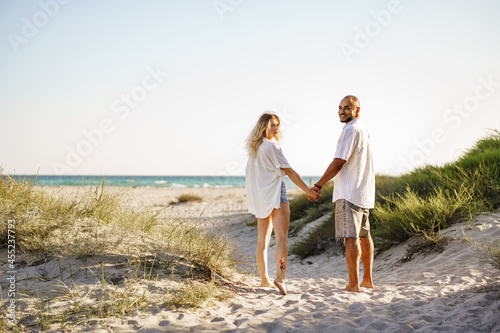 Young happy couple holding hands and walking together to the beach on summer day