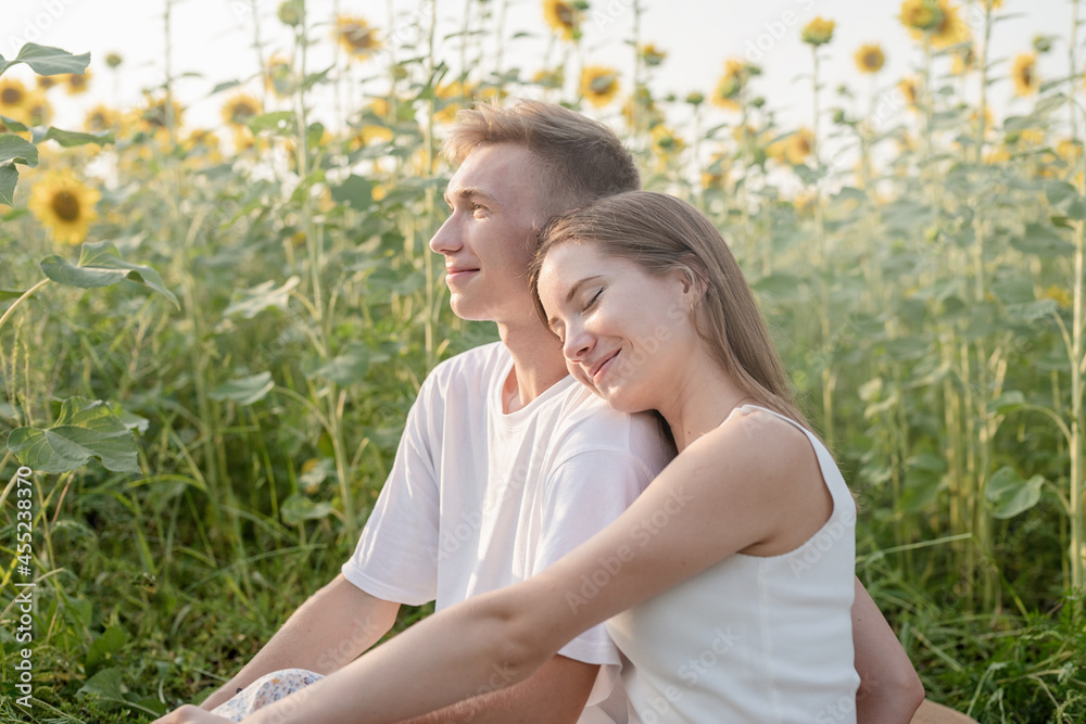 Fototapeta premium Young couple having picnic on sunflower field at sunset, woman lying on boyfriend shoulder