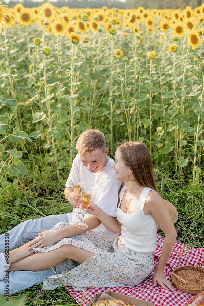 Fototapeta premium Young couple having picnic on sunflower field at sunset