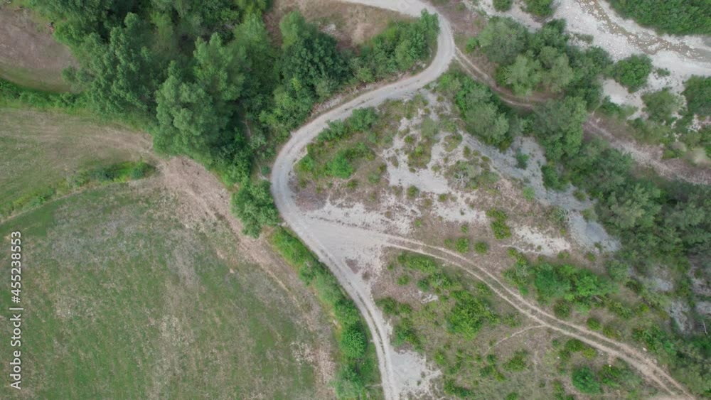 A zig-zag gravel road in the mountains. A dry area with trees and a path winding between the hills. A zig-zag gravel road in the mountains. A dry area with trees and a path winding between the hills.