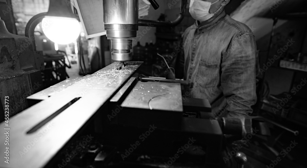 Milling machine working near worker with a protective mask. Tool for cut metal workpiece. Vertical milling machine with cemented carbide milling cutter. Steel manufacturing industry. Milling process. Milling machine working near worker with a protective mask. Tool for cut metal workpiece. Vertical milling machine with cemented carbide milling cutter. Steel manufacturing industry. Milling process.