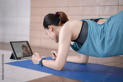 Asian woman in sports outfits worksout following online training program via digital tablet at home