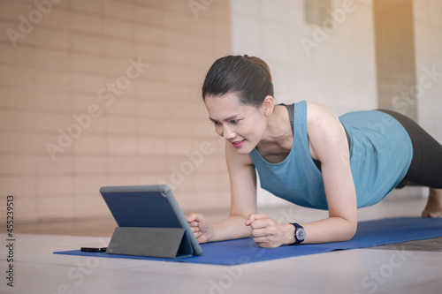 Asian woman in sports outfits worksout following online training program via digital tablet at home