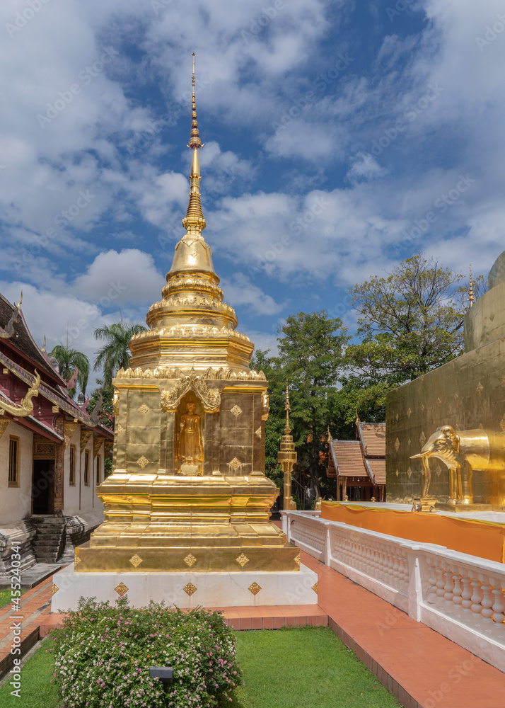 Fototapeta premium Beautiful view of small golden stupa with Buddha statue in niche at famous landmark Wat Phra Singh buddhist temple, Chiang Mai, Thailand