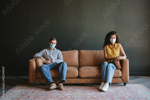 Man and woman in face mask looking at camera while sitting on couch
