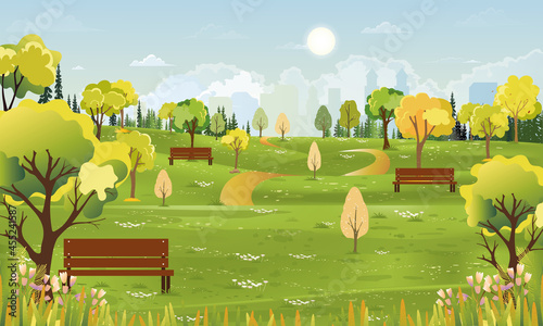 Spring landscape at city park in the morning, Natural public park with flowers blooming in the garden, Peaceful scene of green fields with blurry cityscape building, cloudy and sun on summer