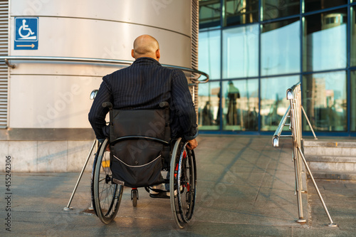 Man wearing jacket riding in wheelchair on ramp by building