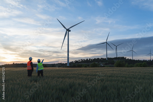 Unrecognized engineers wearing safety helmets working in wind turbine farm during the evening.