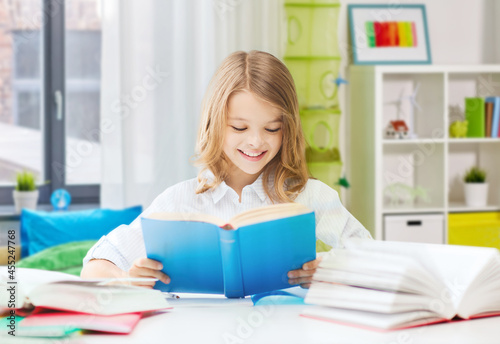 education and school concept - happy smiling student girl reading book over home background