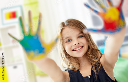 art, creativity and painting concept - happy smiling little girl showing painted hands over home room background
