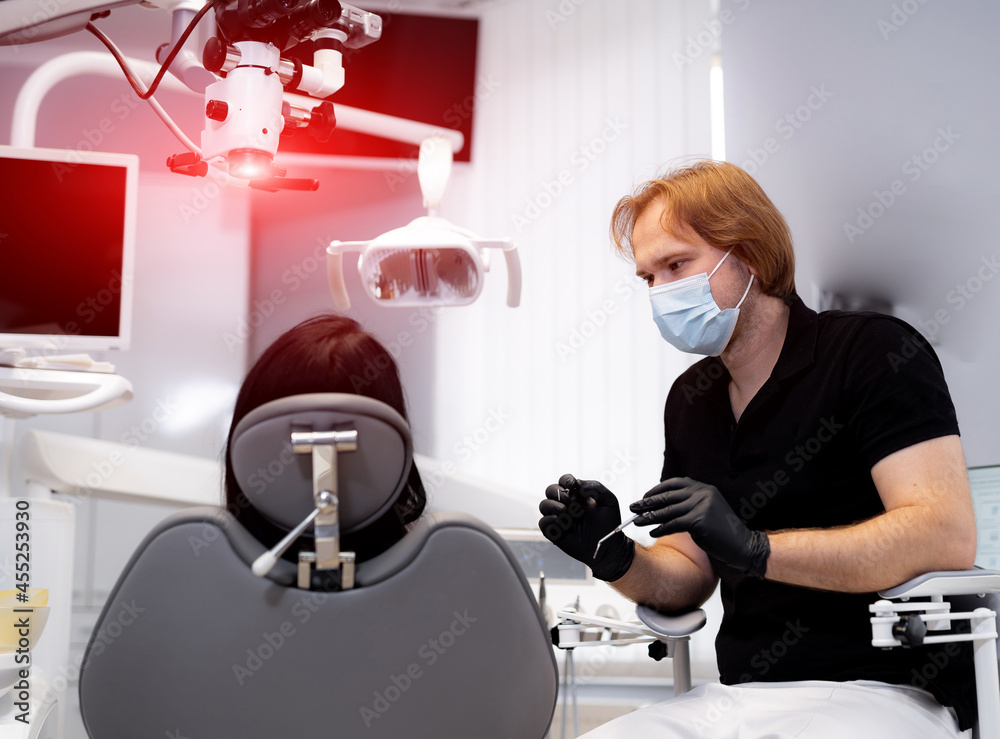 Young medical doctor leaning against chair in hospital. Professional dentist in mask working with patient teeth.