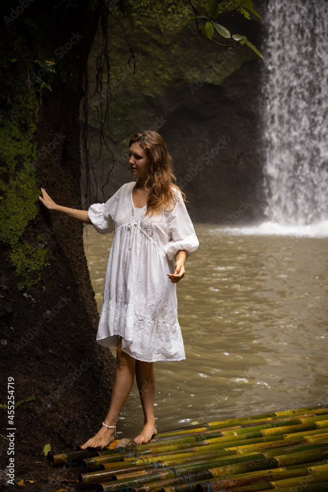 Young woman standing on bamboo raft. Beautiful Caucasian woman wearing white dress. Travel concept. Bali, Indonesia Young woman standing on bamboo raft. Beautiful Caucasian woman wearing white dress. Travel concept. Bali, Indonesia
