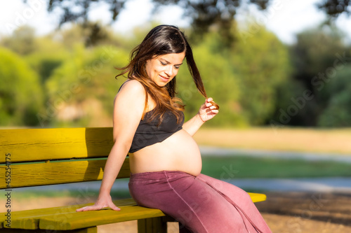 Pregnant woman sitting on a park bench touching her hair in a sunny day © Samuel Perales