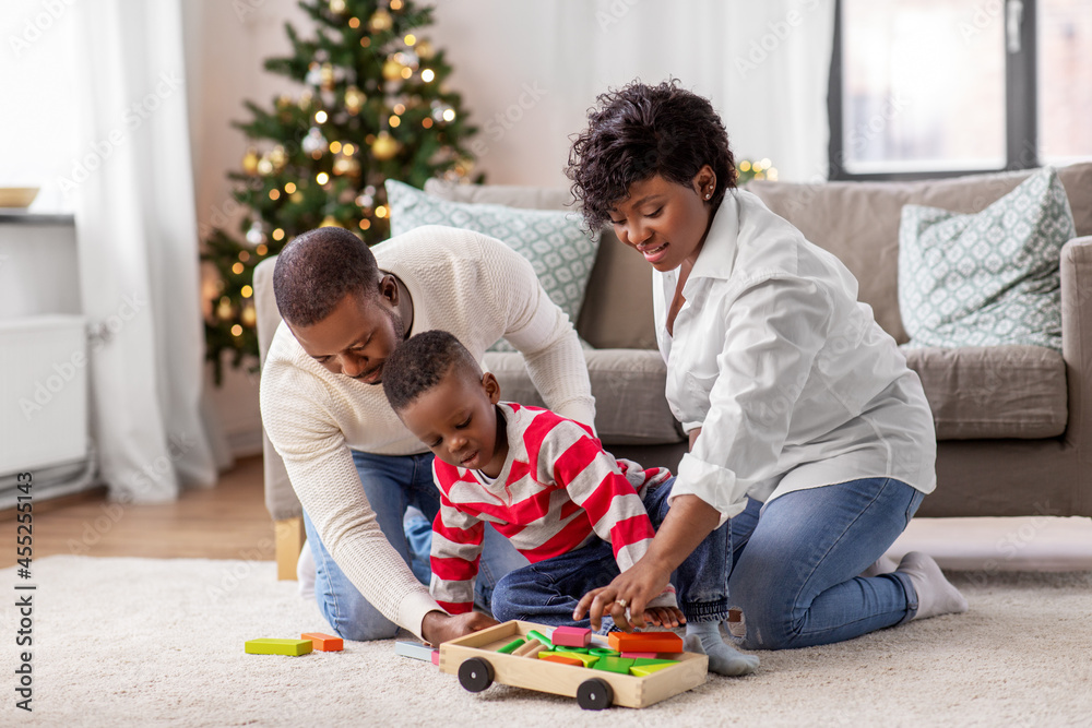 family, winter holidays and people concept - happy african american mother, father and baby son playing with dinosaur and toy blocks at home on christmas family, winter holidays and people concept - happy african american mother, father and baby son playing with dinosaur and toy blocks at home on christmas