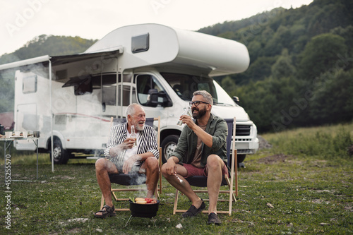 Fototapet Mature man with senior father talking at campsite outdoors, barbecue on caravan holiday trip