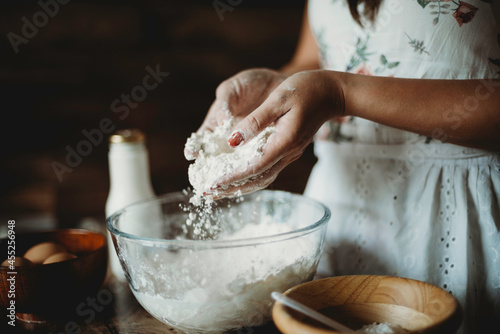 Lady's hands sprinkling and pouring flour into mixing glass bowl.Worker preparing dough.Professional baker in bakehouse.Kneading process.Woman preparing cake baking ingredients.