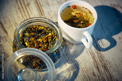 Tea mix of green leaf, flowers, berries and pine nuts in the evening or morning light. Blended tea for brewing on gray wooden background, close up, top view. Herbal medicine, tea drinking culture.