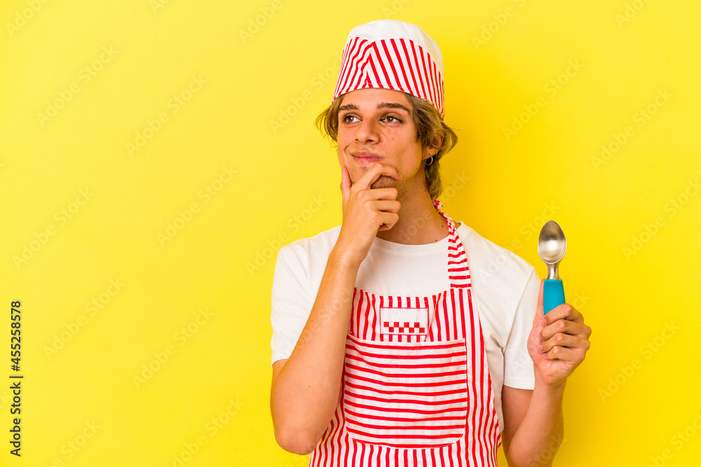 Young ice cream maker man with makeup holding spoon isolated on yellow background looking sideways with doubtful and skeptical expression. Young ice cream maker man with makeup holding spoon isolated on yellow background looking sideways with doubtful and skeptical expression.