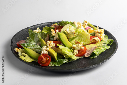 Plate of fresh and healthy summer avocado and tomatoes salad with fresh greenery and popcorn.