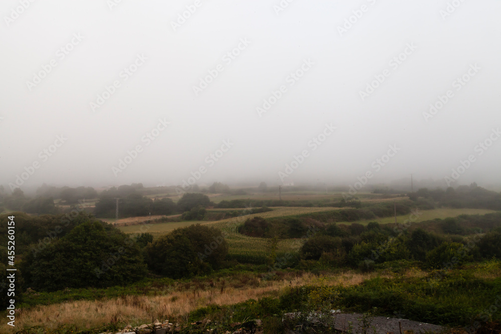 Thick fog falling over San Martiño de Ozon countryside. Landscapes of Galicia with cloudy weather.