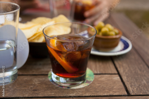 Glass of vermouth alcoholic drink with an orange peel on a tapas bar with olives and chips. Traditional vermouth hour concept.