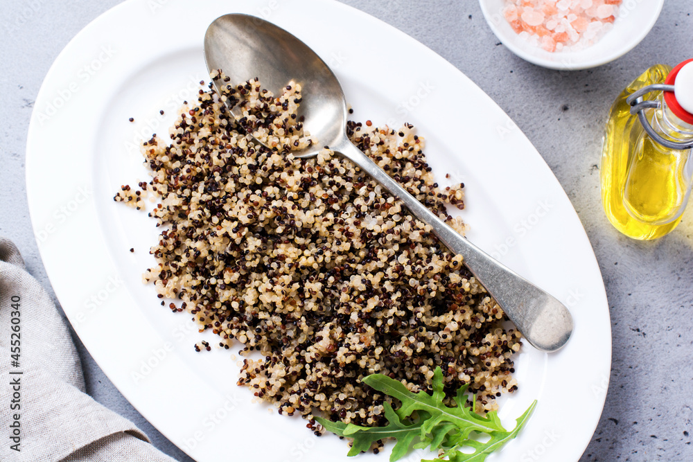 Cooked white, red and black quinoa in white plate on grey rustic background, top view, place for text recipes or menu. Vegan Superfood, healthy eating and nutrition or diet concept. Cooked white, red and black quinoa in white plate on grey rustic background, top view, place for text recipes or menu. Vegan Superfood, healthy eating and nutrition or diet concept.