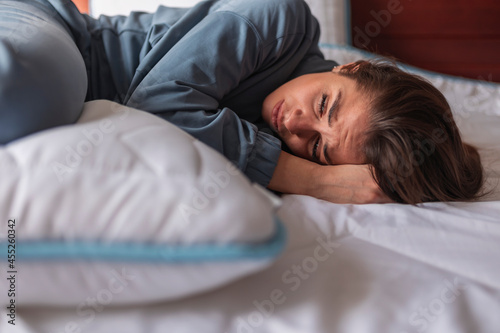 Curled up woman lying in bed having menstrual cramps