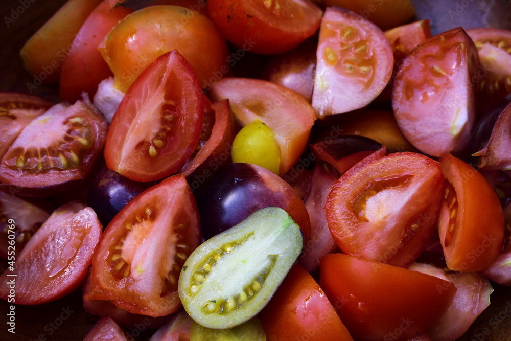 Geschnittene Tomaten in Hälften und Vierteln, verschiedene Sorte in Holzschüssel in Rot, Gelb, Violett Geschnittene Tomaten in Hälften und Vierteln, verschiedene Sorte in Holzschüssel in Rot, Gelb, Violett