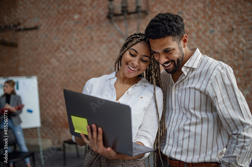 Cheerful young businesspeople with laptop working in office, cooperation concept.