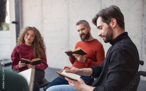 Men and women sitting in circle reading Bible book during group therapy. © Halfpoint