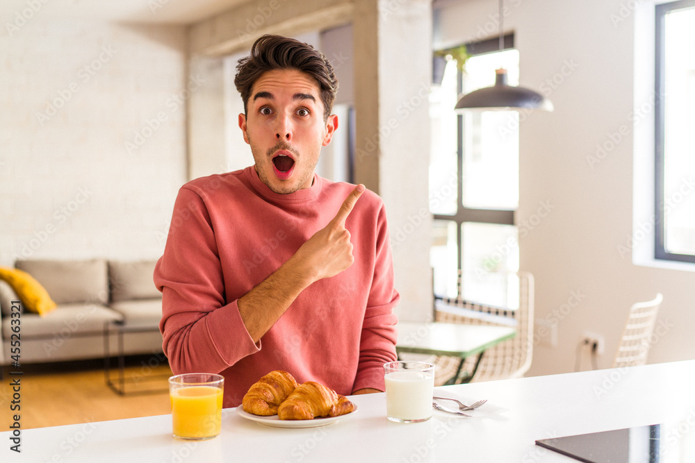 Young mixed race man having breakfast in a kitchen on the morning pointing to the side Young mixed race man having breakfast in a kitchen on the morning pointing to the side