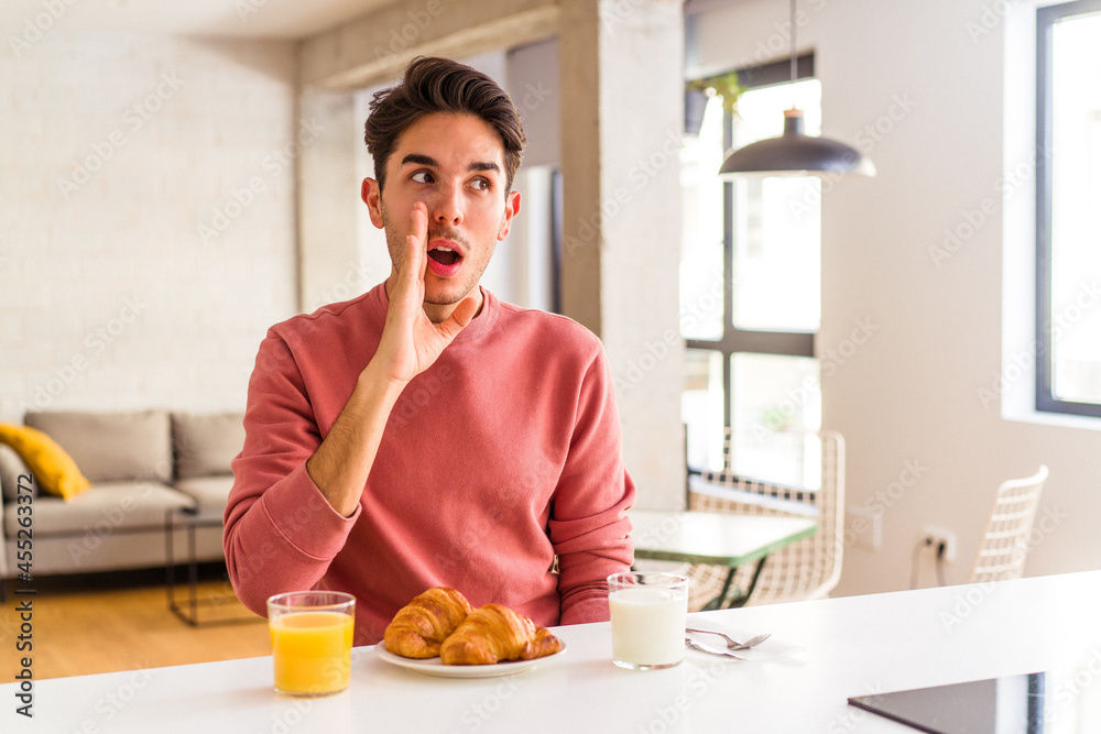 Young mixed race man having breakfast in a kitchen on the morning is saying a secret hot braking news and looking aside Young mixed race man having breakfast in a kitchen on the morning is saying a secret hot braking news and looking aside