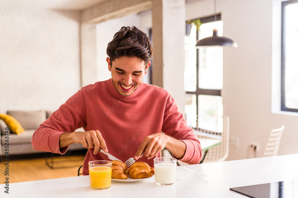 Young mixed race man eating croissant in a kitchen on the morning Young mixed race man eating croissant in a kitchen on the morning