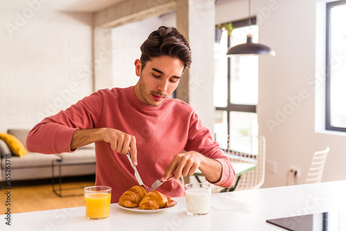 Young mixed race man eating croissant in a kitchen on the morning