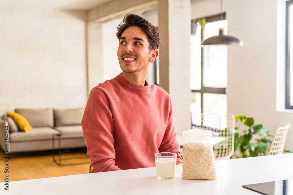 Young mixed race man eating oatmeal and milk for breakfast in his kitchen looks aside smiling, cheerful and pleasant. Young mixed race man eating oatmeal and milk for breakfast in his kitchen looks aside smiling, cheerful and pleasant.