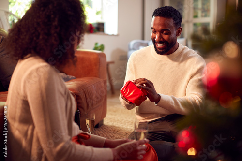 Loving Couple Opening Gifts Around Christmas Tree At Home