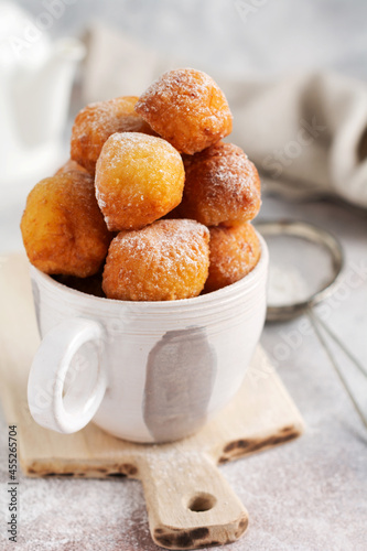 Little Donuts. Home-made cottage cheese cookies deep-fried and sprinkled with icing sugar in a vintage ceramic cup on a light background. Selective focus