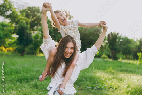 Happy excited young woman in white clothes have fun with cute child baby girl 5-6 years old Mommy play rest with little kid daughter sitting on neck outdoor together Mother's Day love family concept